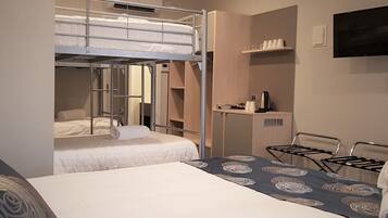 A hotel room with a bunk bed, a desk with a kettle, a TV, and a shelf with cups.