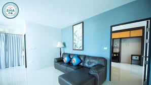 A modern living room with a dark leather sofa, a standing lamp, and a framed artwork on the wall. - Lee Hotel (Surat Thani)