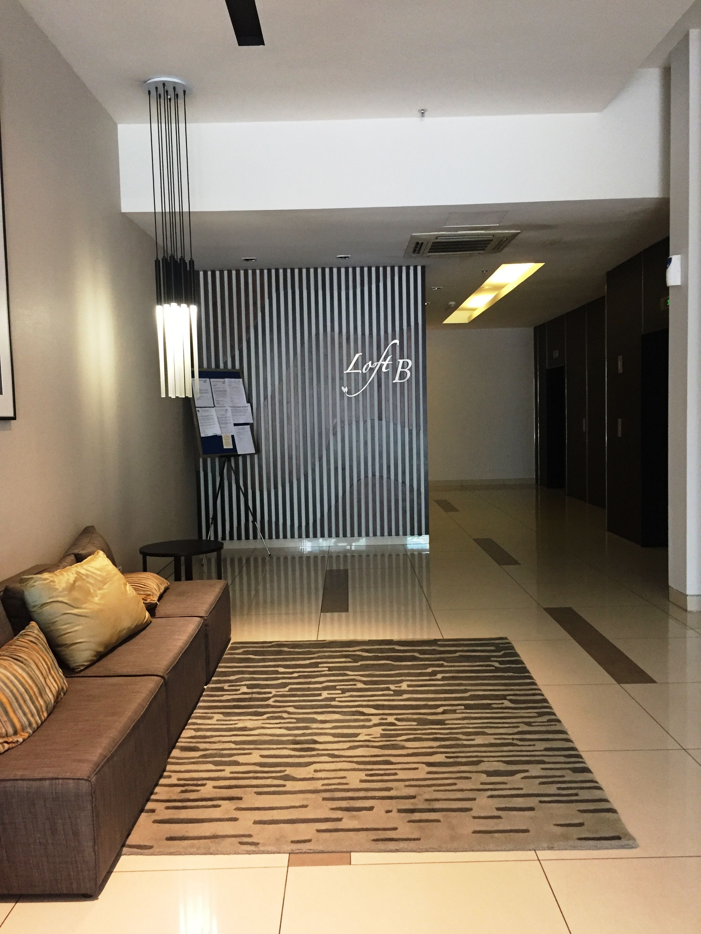 A modern lobby with a sofa, a patterned rug, and a wall with vertical lines and the text "Loft B".