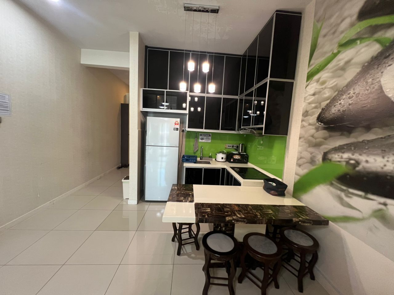 A modern kitchen with a white refrigerator, a dining table with four stools, and a green backsplash.