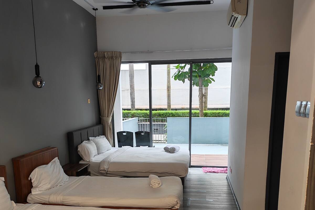 Habitación de hotel con tres camas, ventilador de techo y vistas al exterior.
