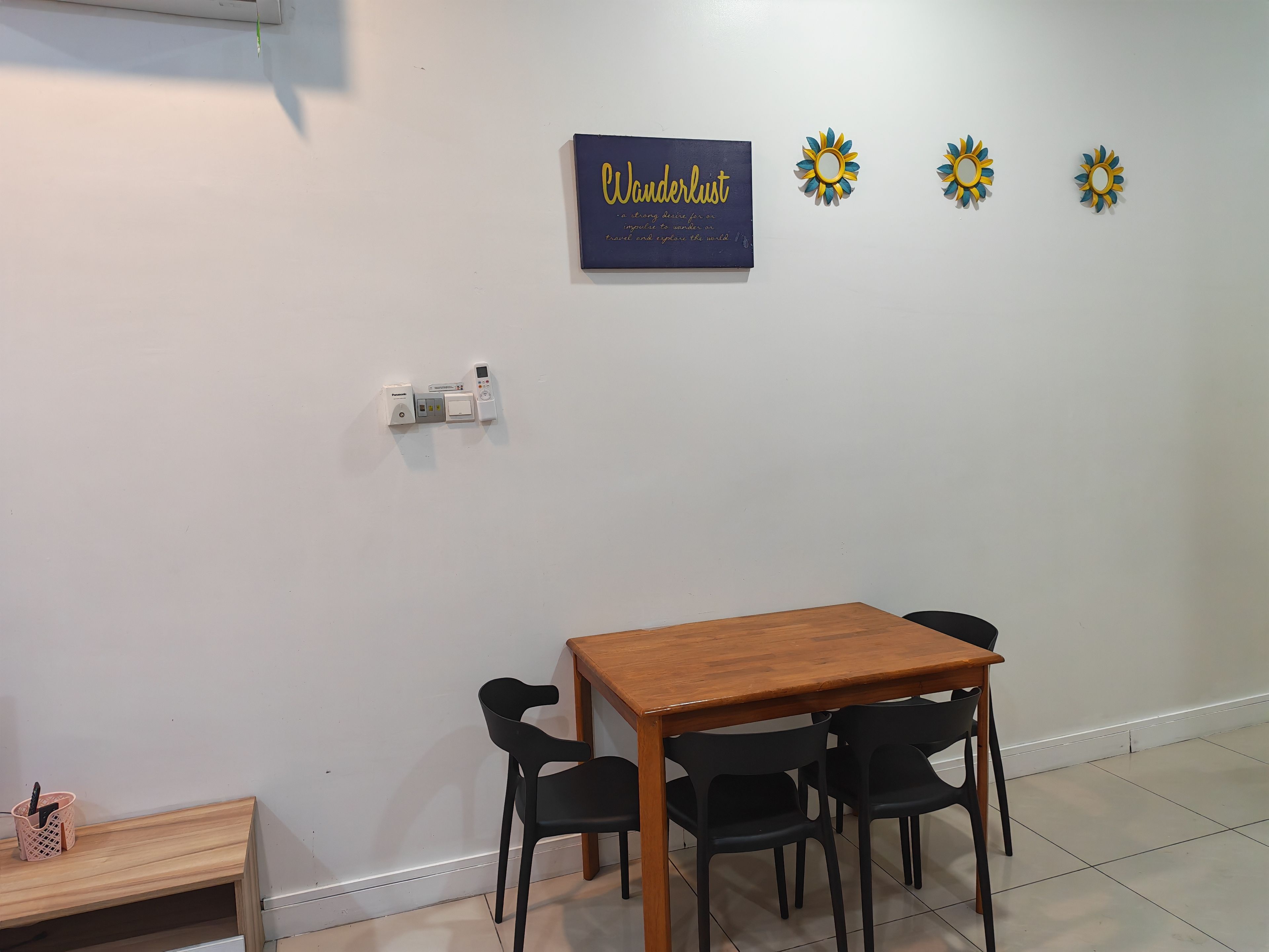 A room with a wooden table and four chairs, a wall-mounted thermostat, and three sunflowers.