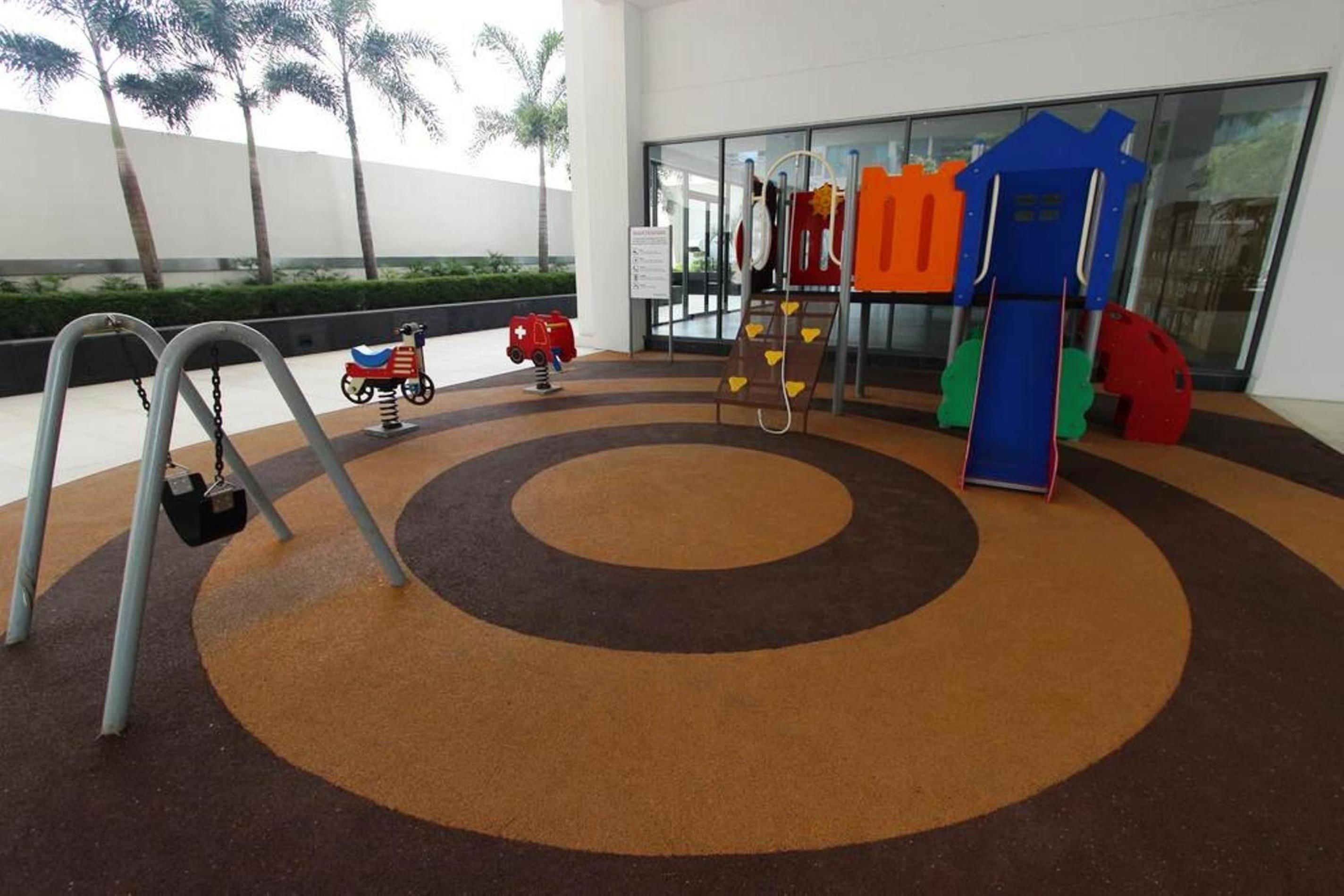 An indoor play area with a circular carpet design, a swing set, and colorful play structures.