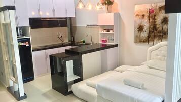A compact hotel room with a kitchenette, a bed with white bedding, and a painting on the wall.