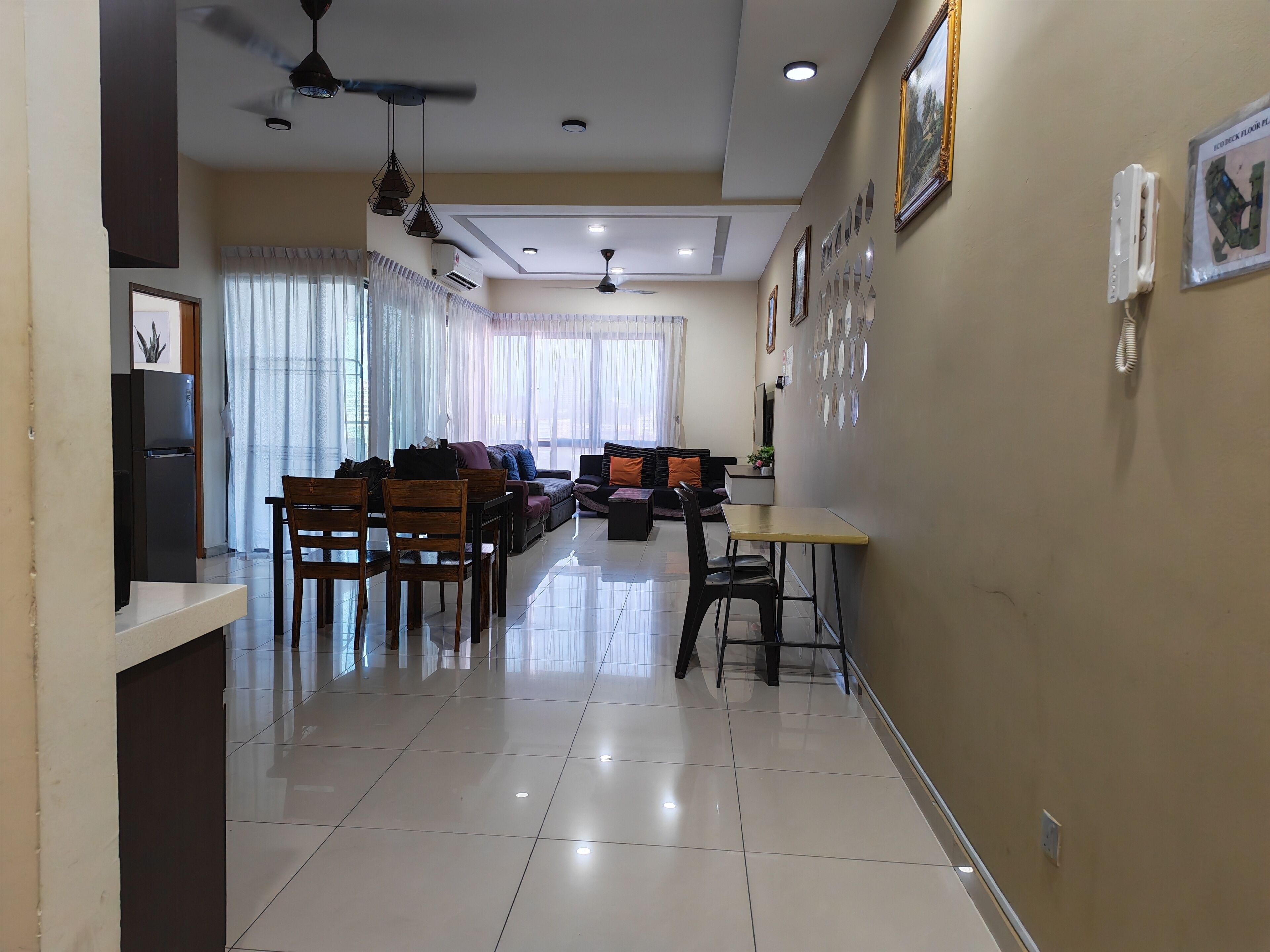 A modern living room with a dining area, a black refrigerator, and a ceiling fan.