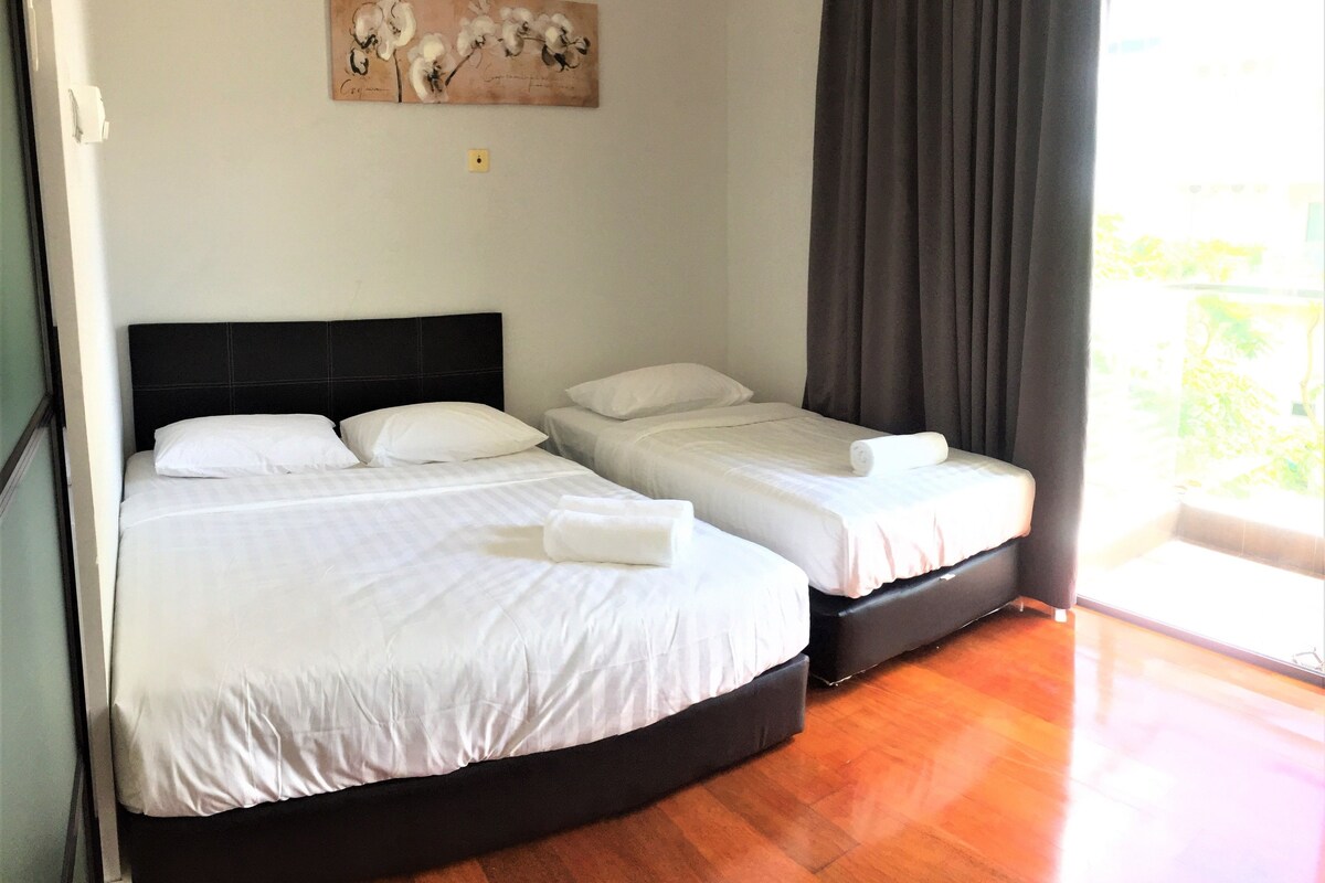 A hotel room with a large bed, two smaller beds, a painting on the wall, and a view of greenery outside.