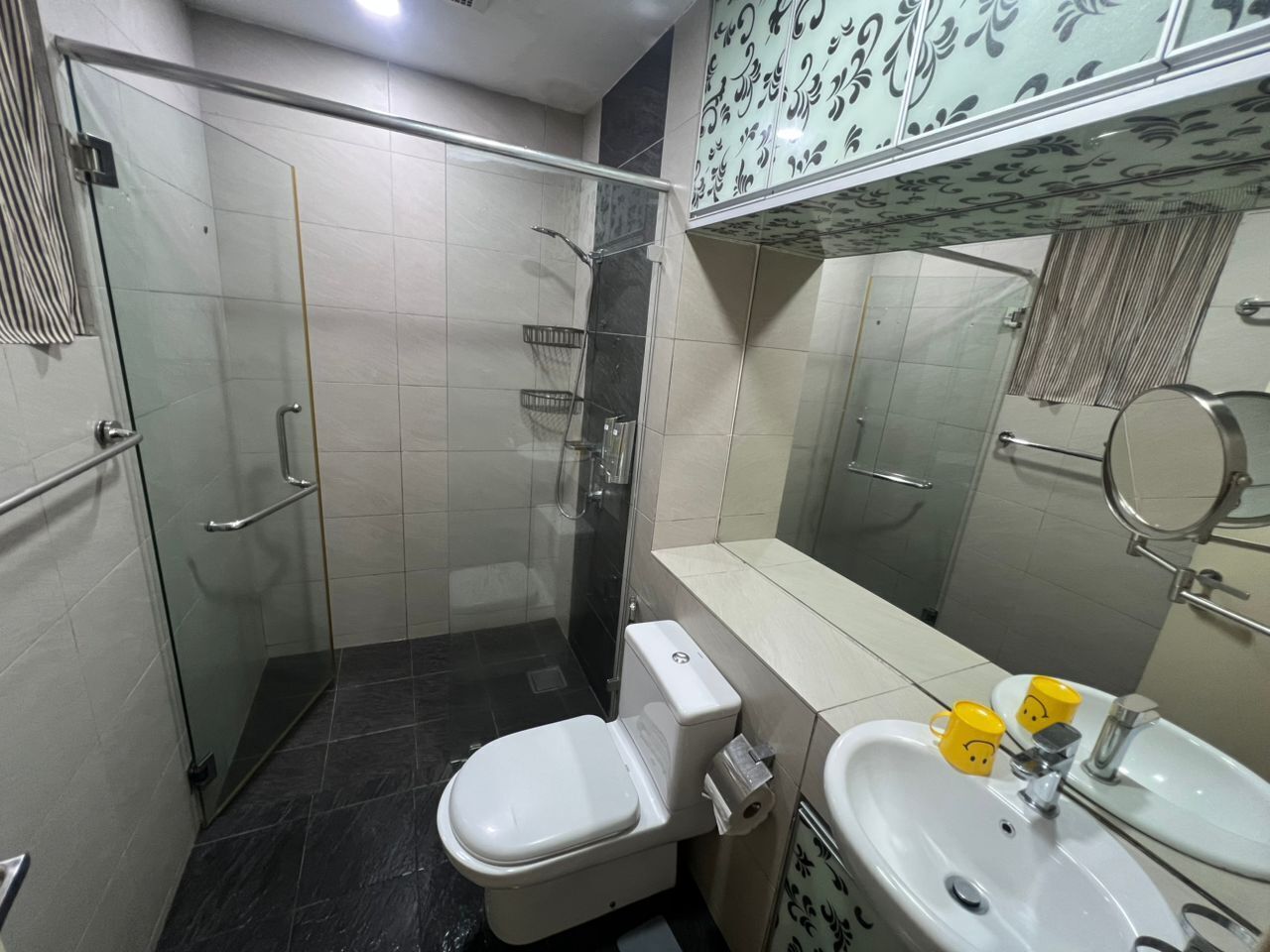 Een badkamer met een douchecabine van glas, een toilet, een wastafel en een spiegel.