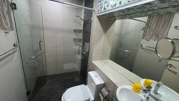 Een badkamer met een douchecabine van glas, een toilet, een wastafel en een spiegel.