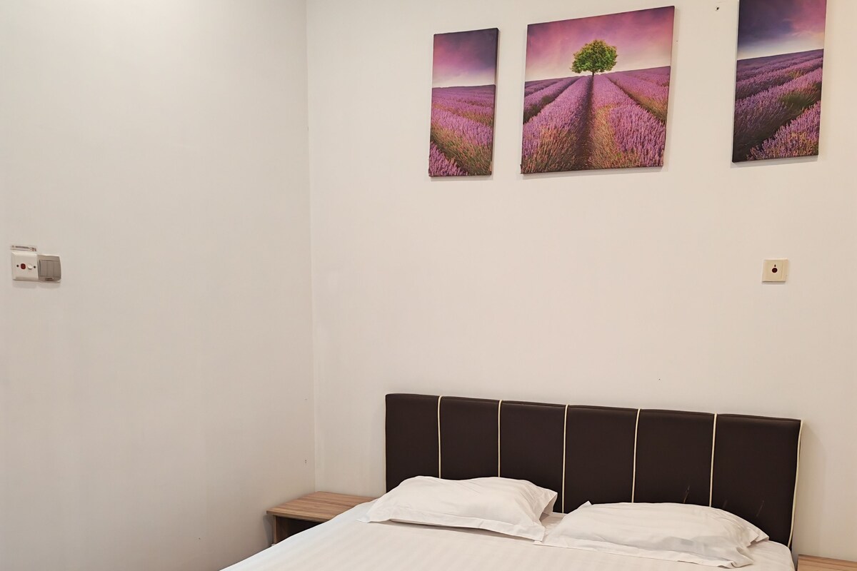 A neatly made bed with white linens and two rolled towels, a dark headboard, and three landscape paintings on the wall.