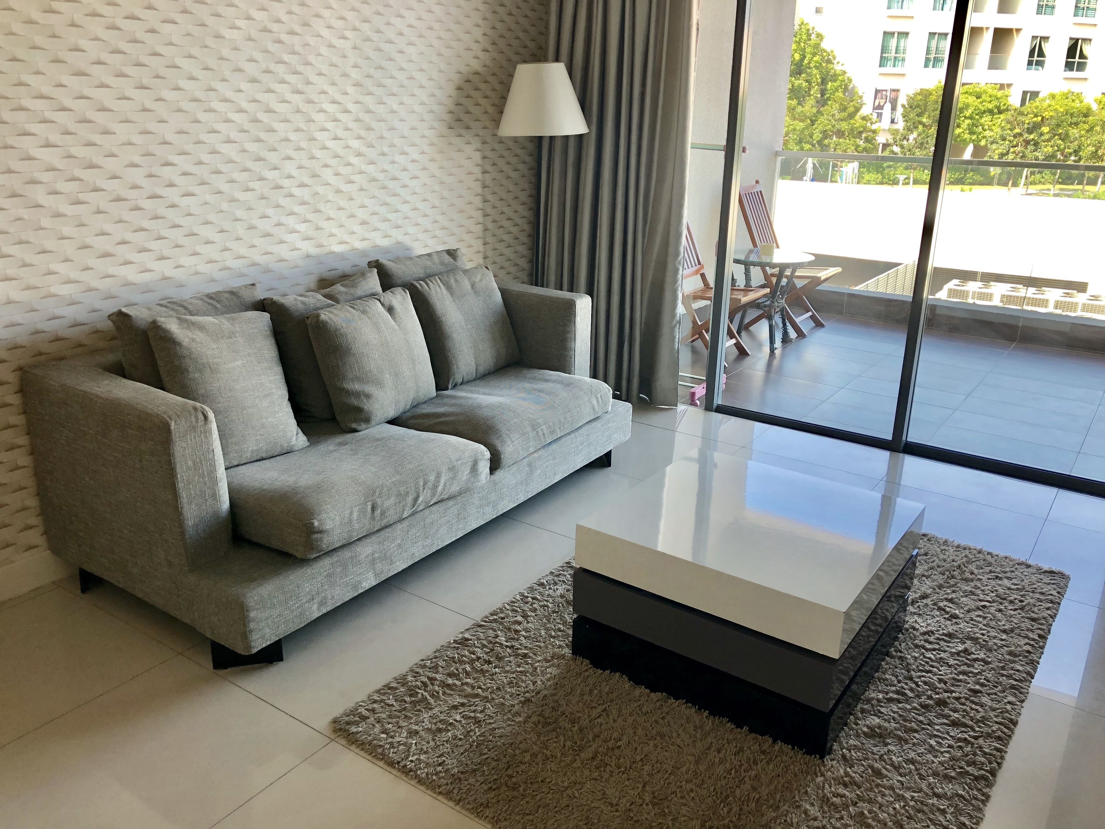 Una sala moderna con un sofá gris, una mesa de centro de vidrio y un papel tapiz estampado.