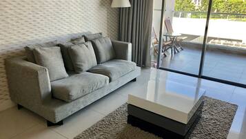Una sala moderna con un sofá gris, una mesa de centro de vidrio y un papel tapiz estampado.