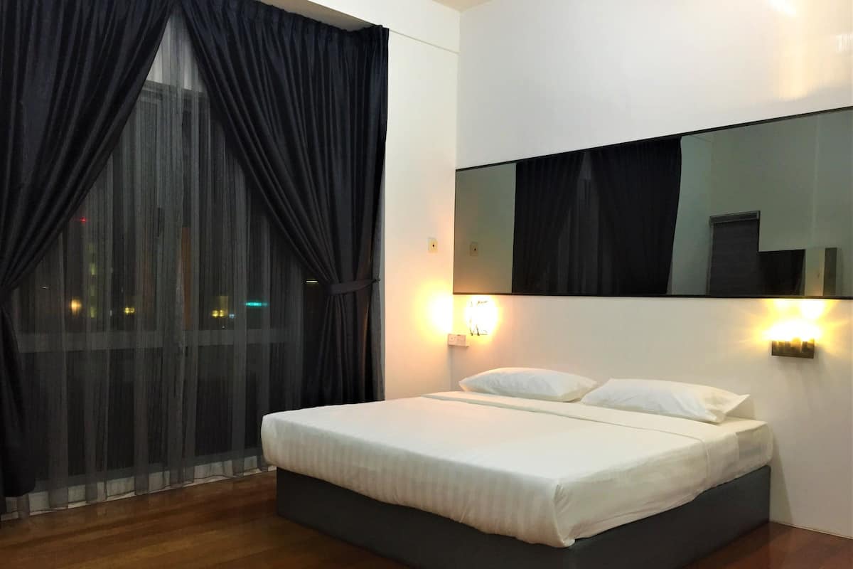 Una habitación de hotel moderna con una cama grande, cortinas oscuras, un espejo amplio y dos luces fijadas a la pared.
