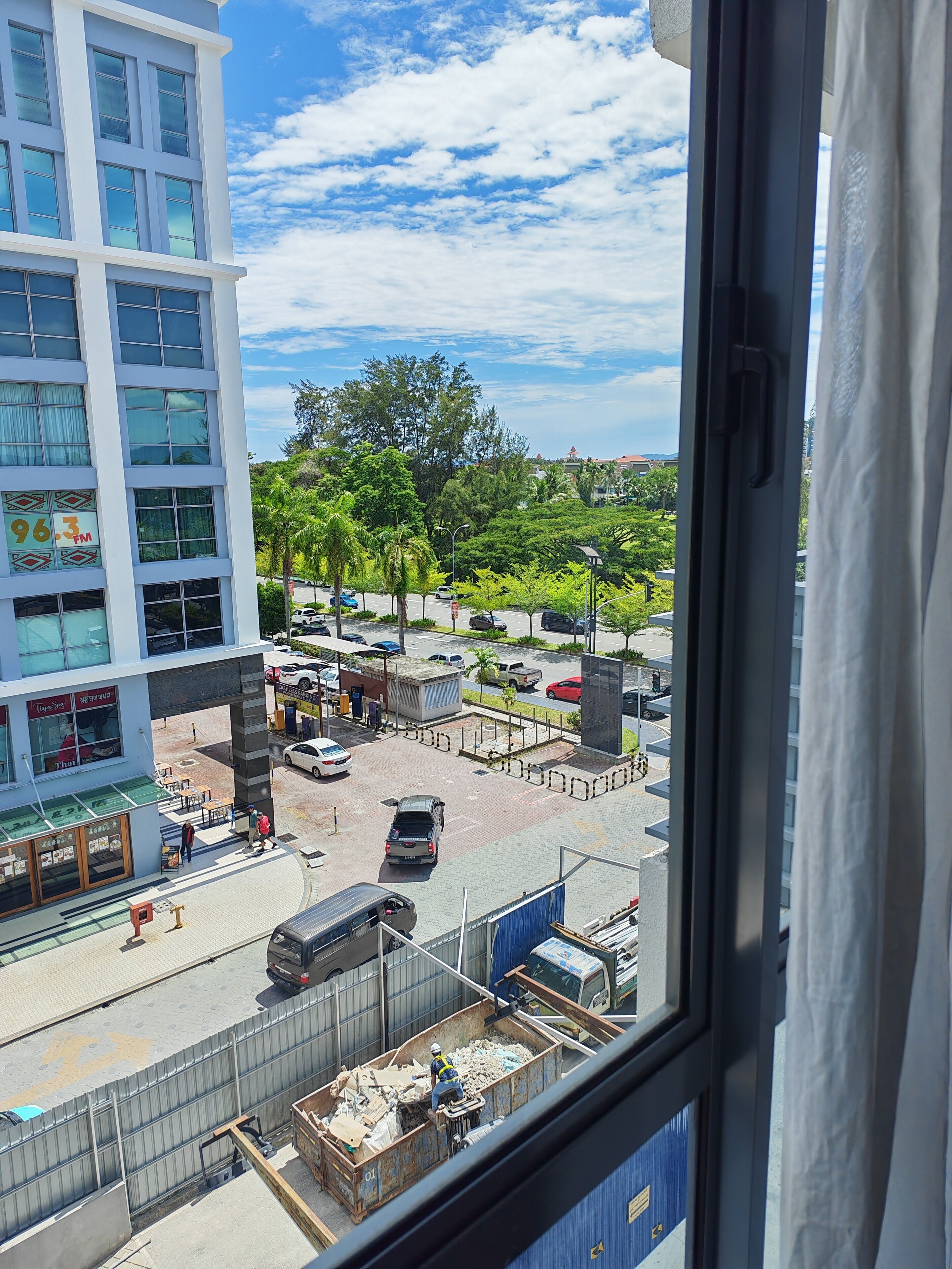 A view of a busy street with buildings, a parking lot, and a worker near a dumpster.