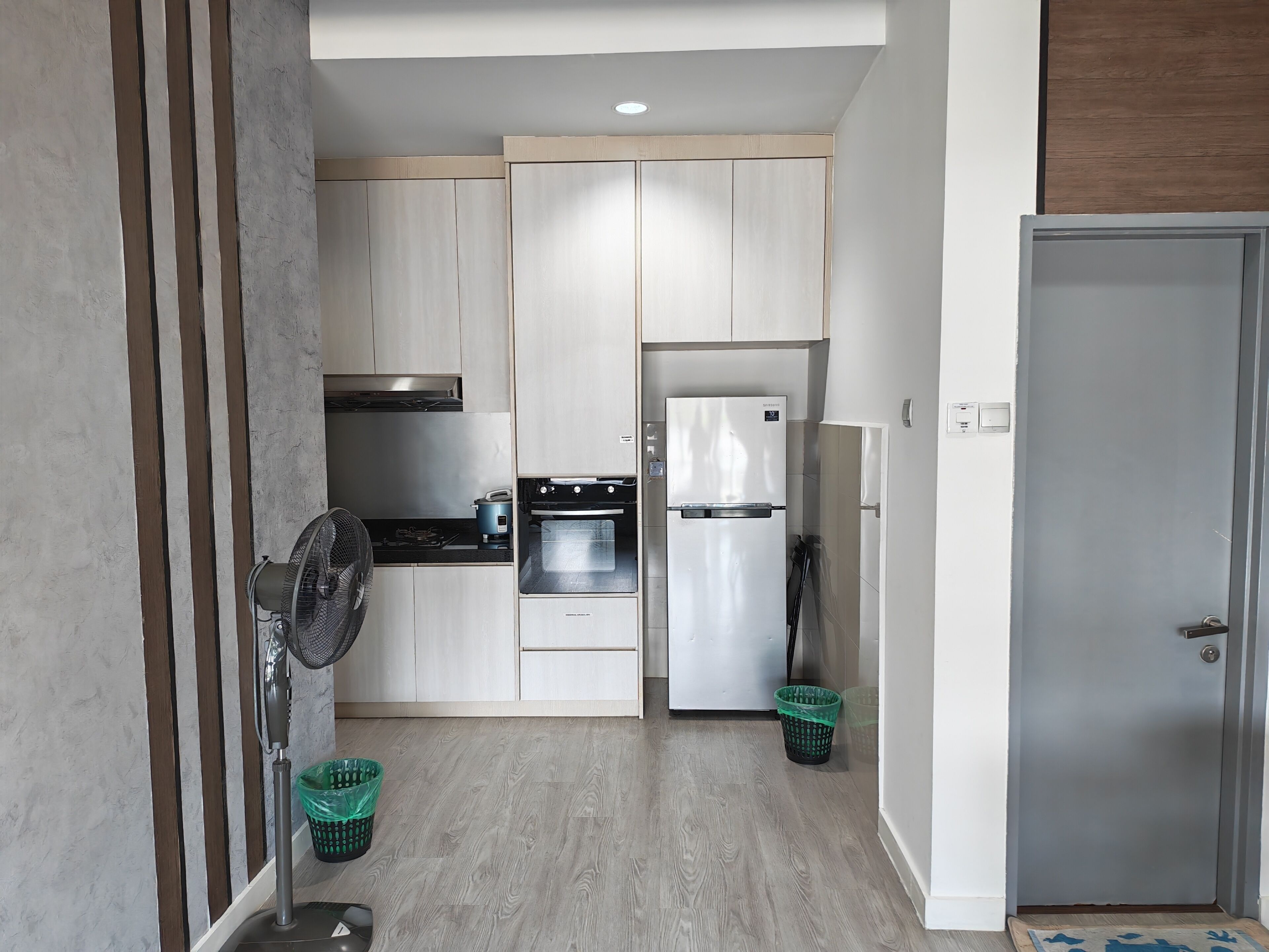A modern kitchen with a stove, oven, and refrigerator, wooden cabinets, and a fan.