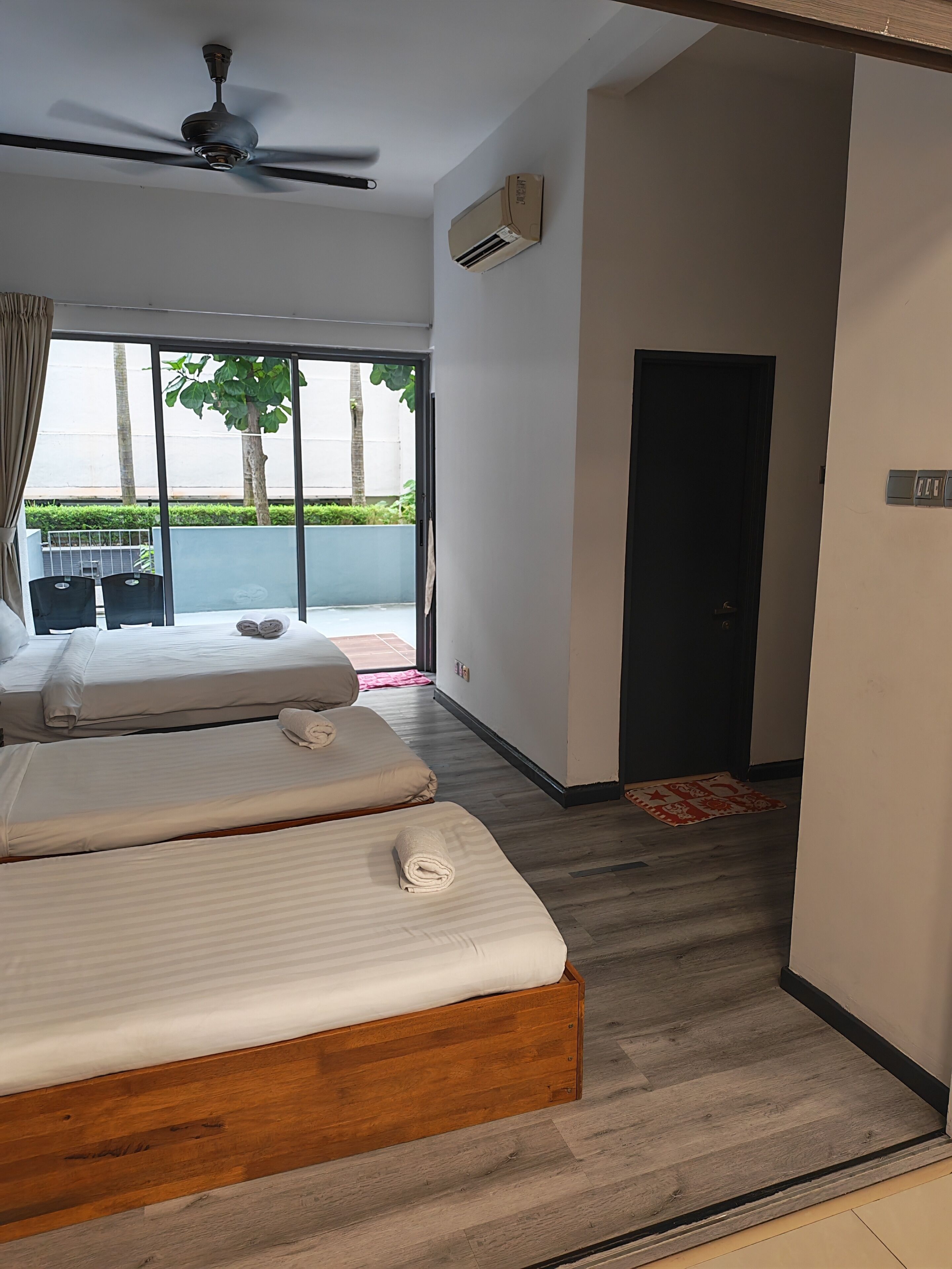 A hotel room with two beds, a ceiling fan, an air conditioning unit, and a view of the outdoors.