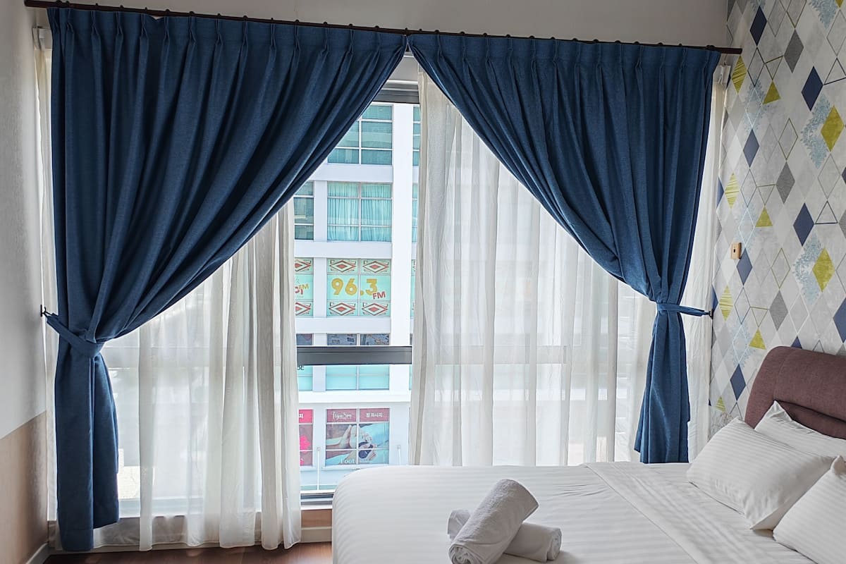 Una habitación de hotel con una cama, una ventana con cortinas azules y vistas a edificios.