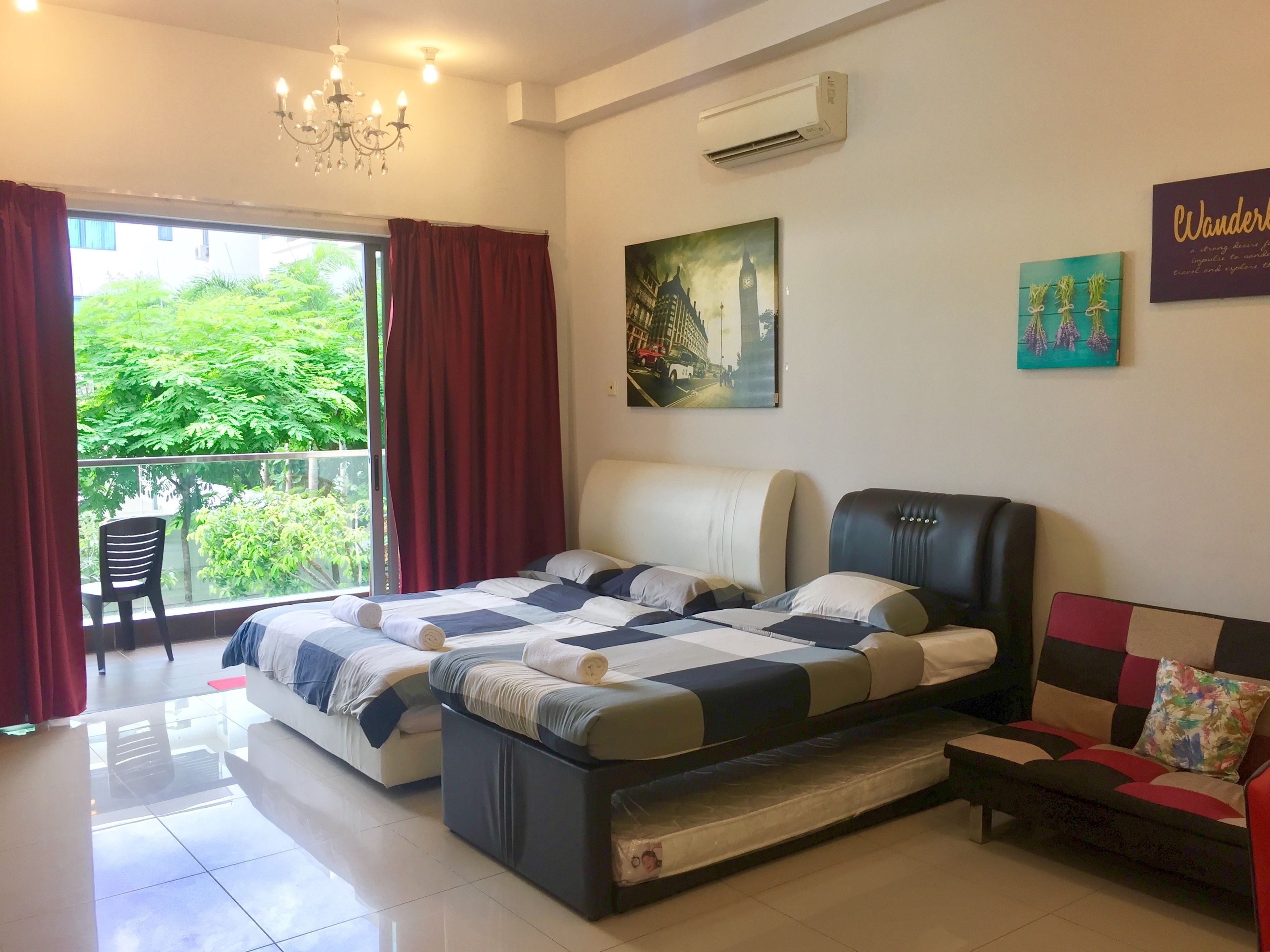 A hotel room with a bed, a sofa, a chair, a painting, and an air conditioning unit.