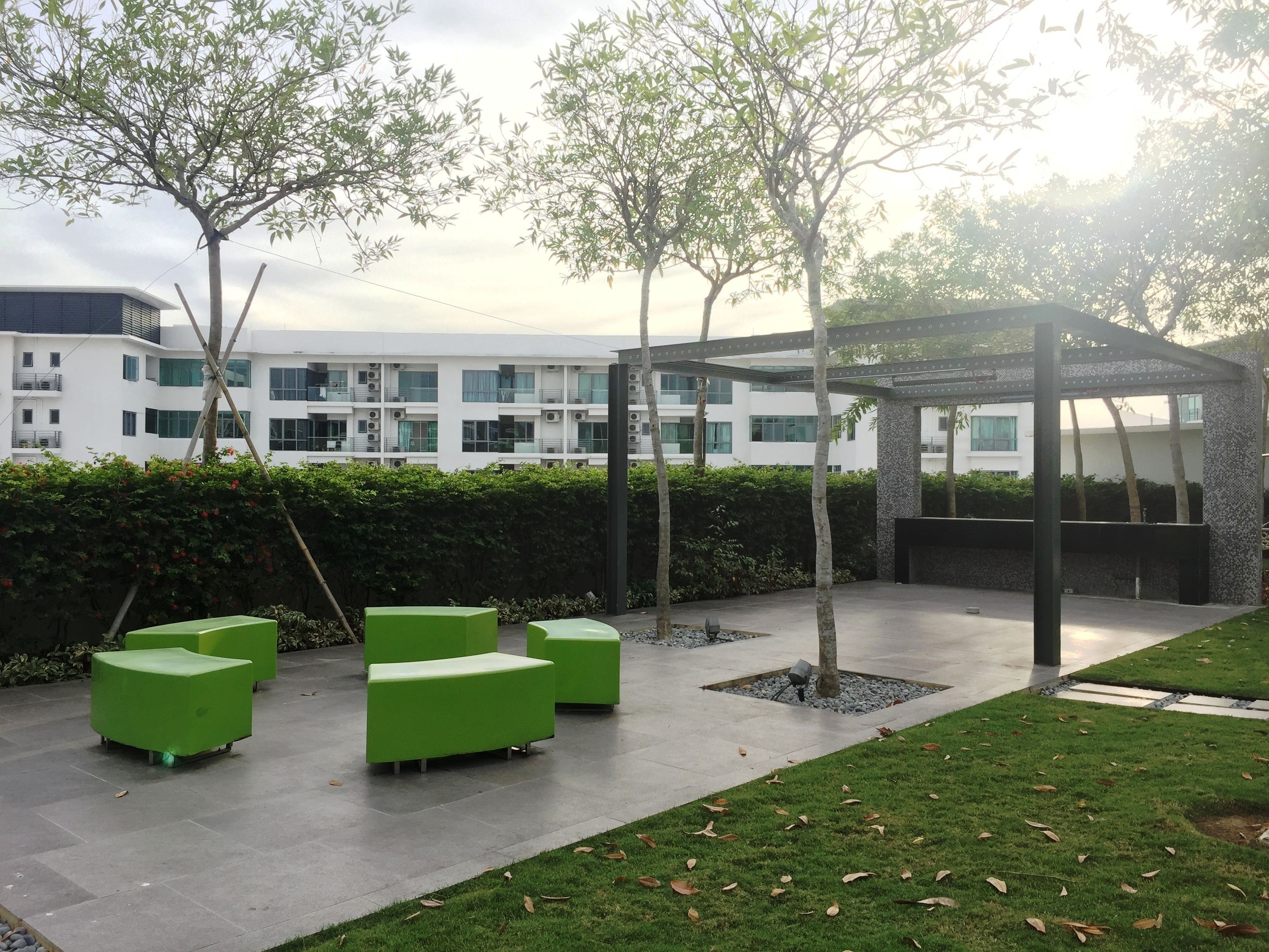 Un patio con asientos verdes, árboles y un edificio moderno al fondo.