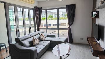 A modern living room with a grey sofa, a round coffee table, a ceiling fan, and a large window with curtains.