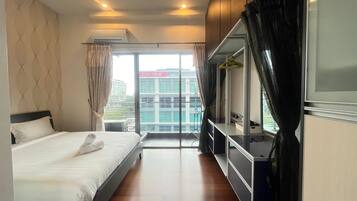 A hotel room with a bed, a desk, a chair, a ceiling fan, and a view of buildings outside.