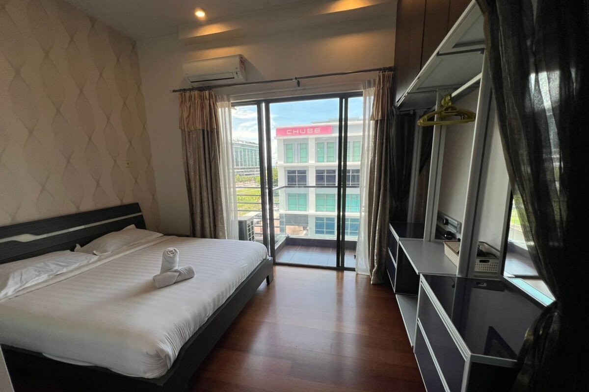 A hotel room with a bed, a TV, and a balcony with a view of a building.