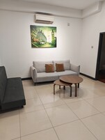 Ein Zimmer mit einem grauen Sofa, einem runden Couchtisch und einem Stadtbild als Gemälde.