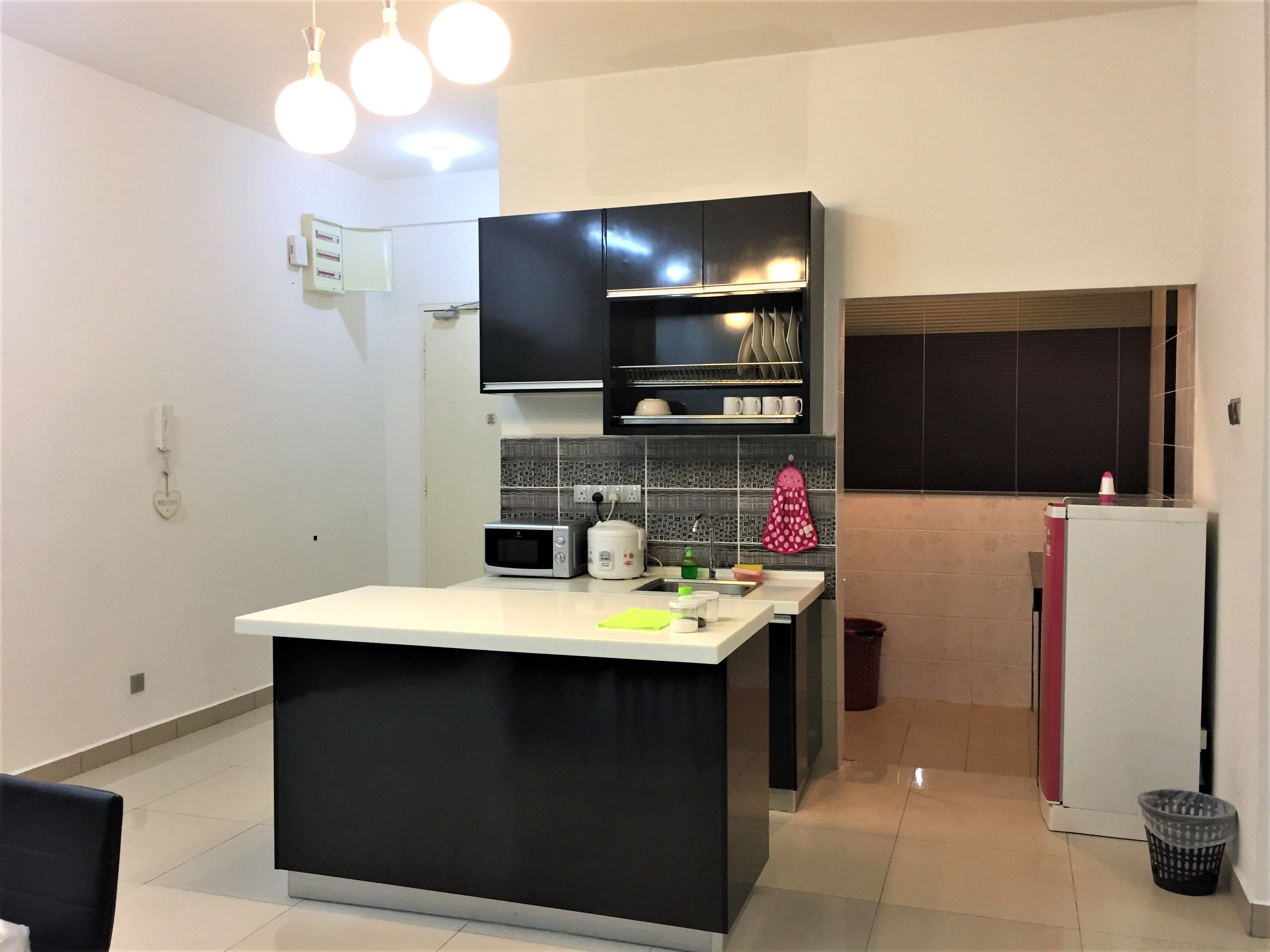 A modern kitchen with a central island, black cabinets, a microwave, a kettle, and a sink.