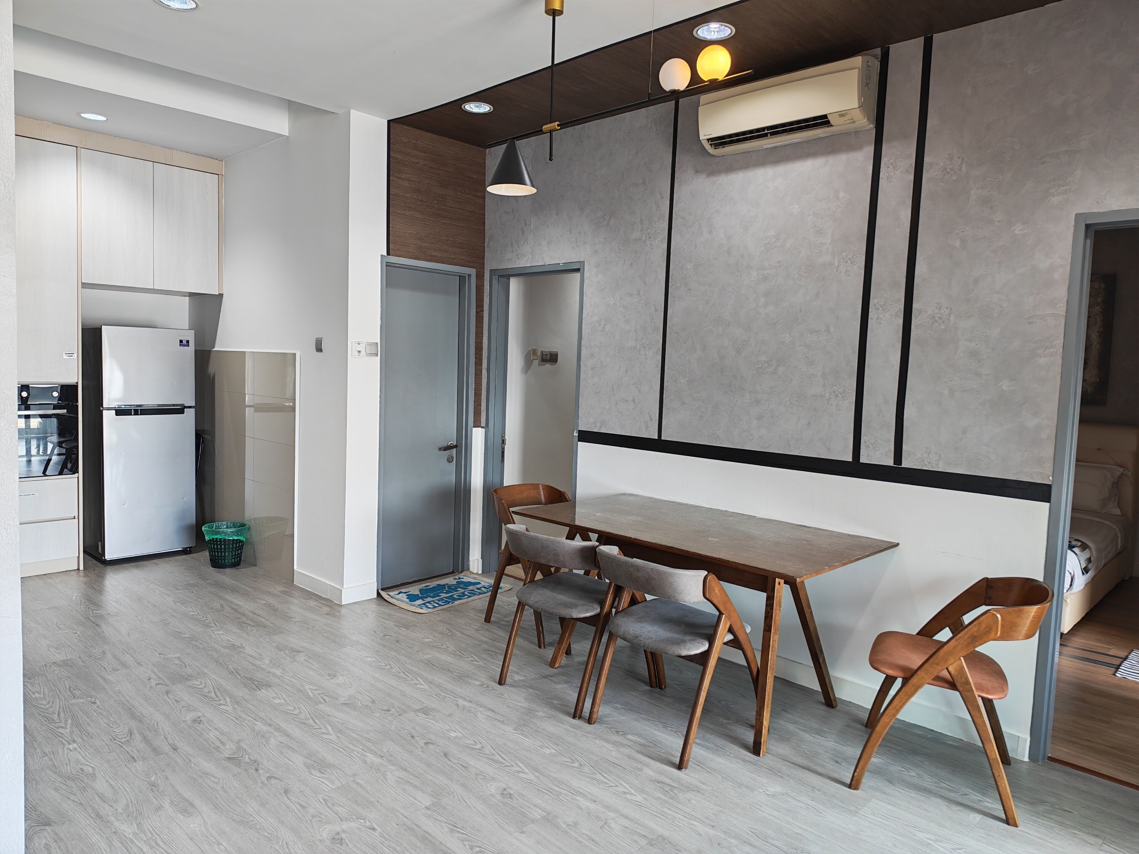 A modern kitchen with a built-in refrigerator, a dining area with a wooden table and chairs, and an air conditioning unit on the wall.
