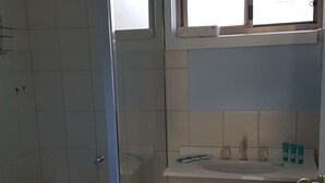 Kylpyhuoneessa on lasiseinällä varustettu suihku, ikkunan yläpuolella oleva pesuallas sekä kaappi, jossa on pyyhe roikkuvana.