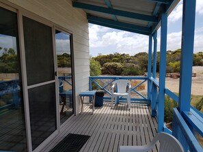 Un espace extérieur abrité doté d’une terrasse en bois, d’une porte-fenêtre coulissante, d’une chaise en plastique blanche et d’une petite table.