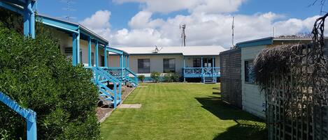 A row of blue-roofed cabins with a well-maintained lawn and a telephone tower in the background.