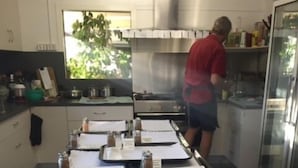 A kitchen with multiple baking trays lined up, a person working in the background, and various kitchen utensils and appliances.