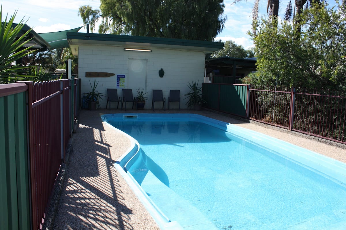 Piscina com uma estrutura no telhado verde, cercada por uma grade e vasos de plantas.