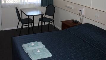 A hotel room with a bed, a desk, a chair, a small table, and a telephone.