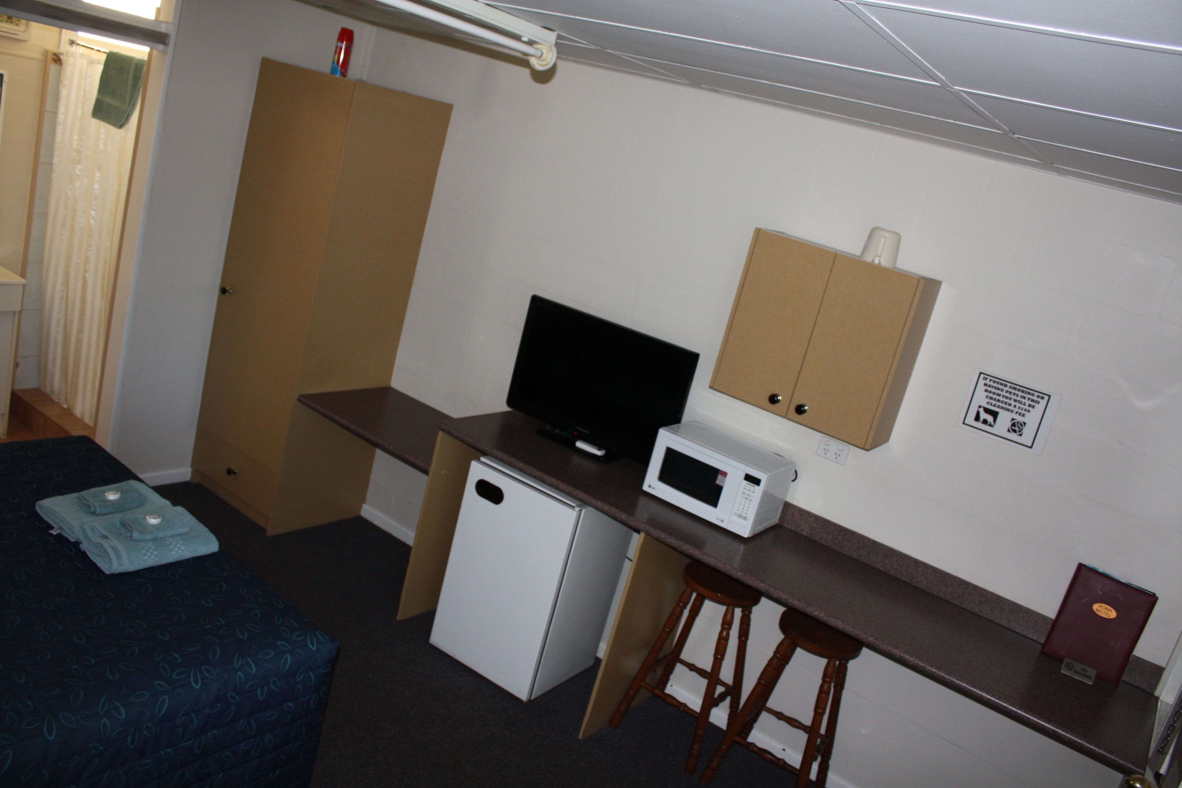 Een compacte hotelkamer met een bed, een kleine kitchenette, een televisie, een magnetron en een houten kruk.