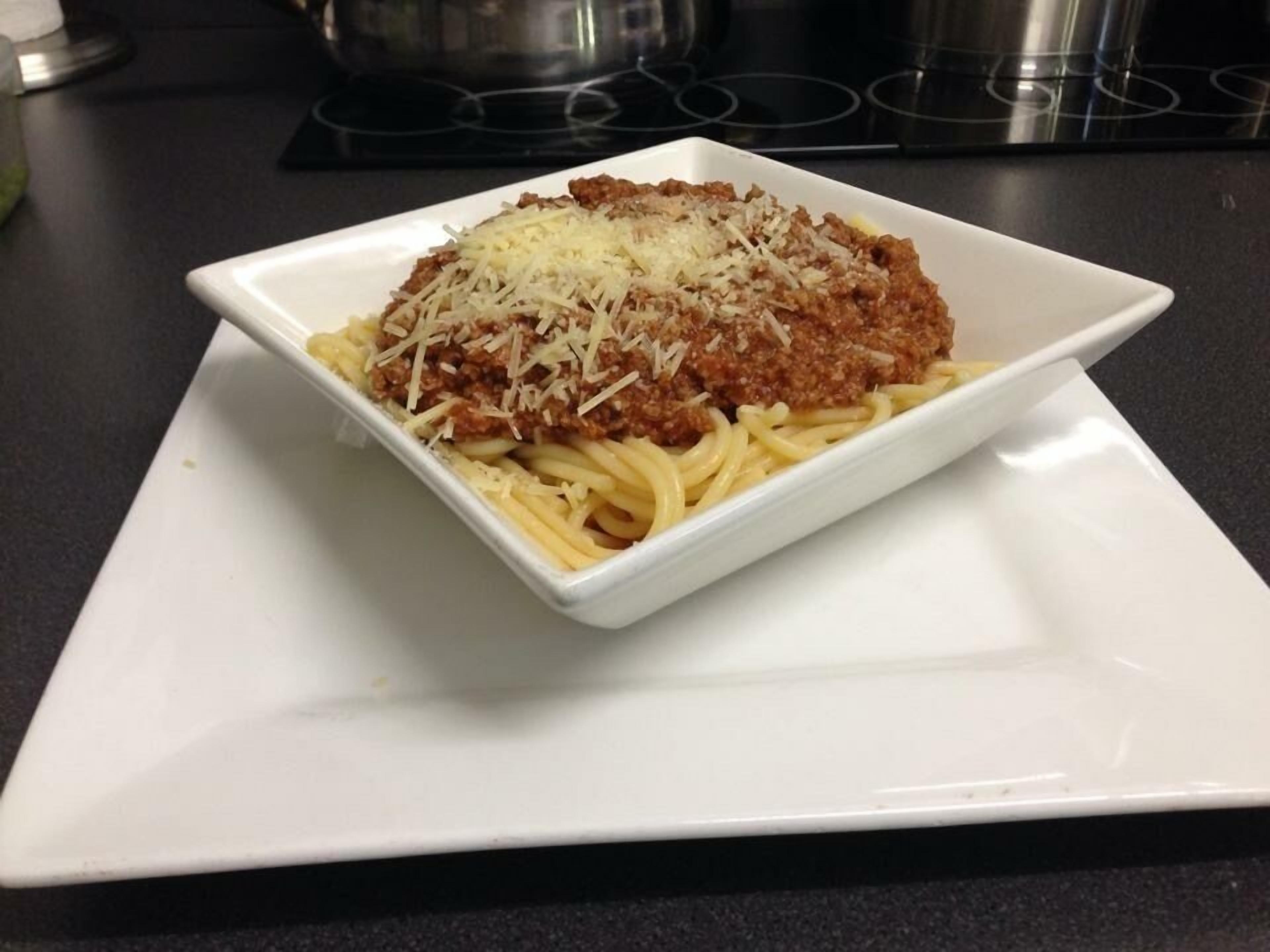 A square white plate with a serving of spaghetti topped with tomato sauce and grated cheese.