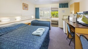A hotel room with two beds, a desk with a TV, and a view of the outdoors.