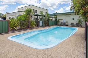A rectangular swimming pool with a pebble border, surrounded by a fence and greenery.