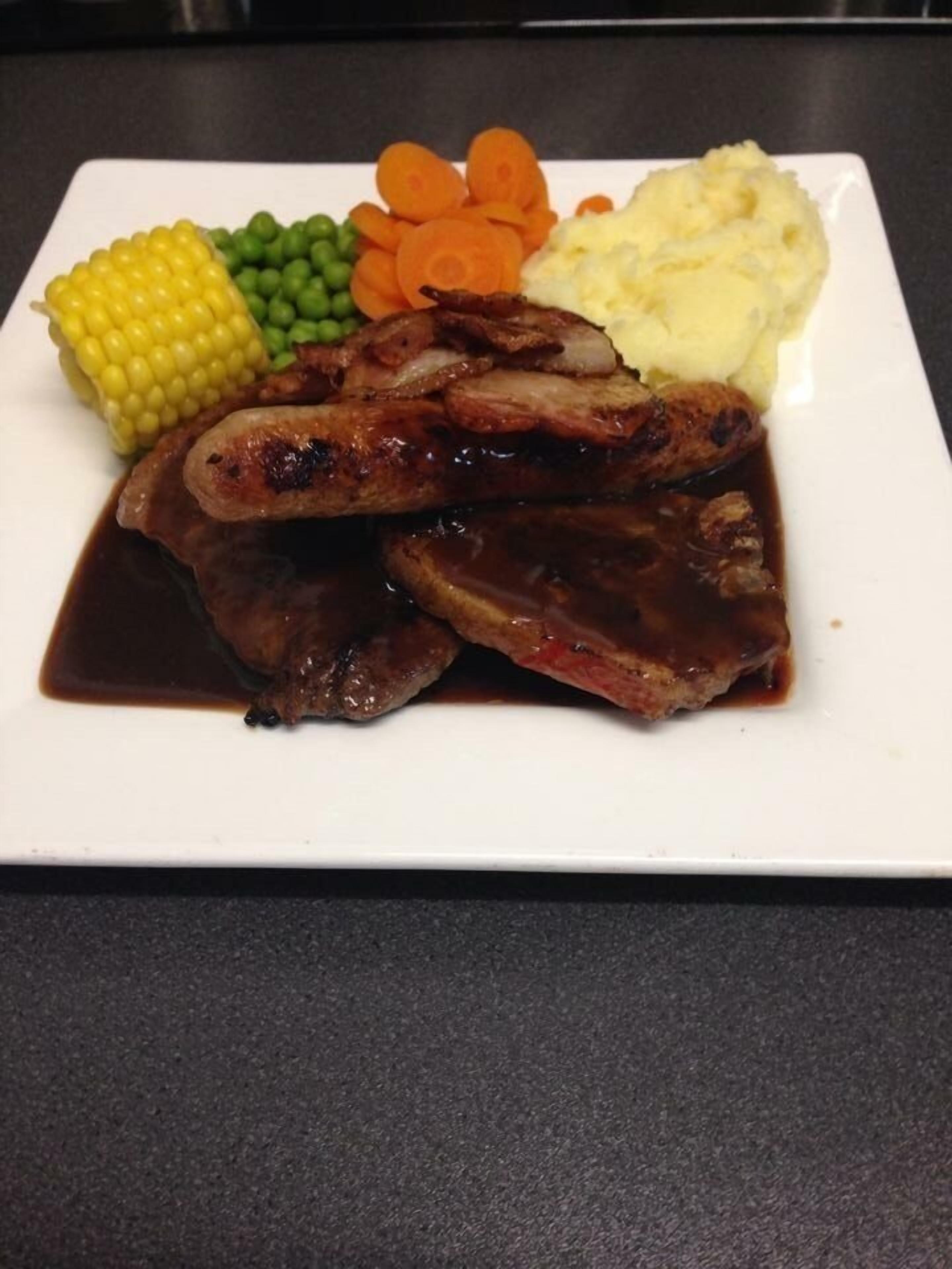 A plate with ribs, mashed potatoes, corn, peas, and carrots.