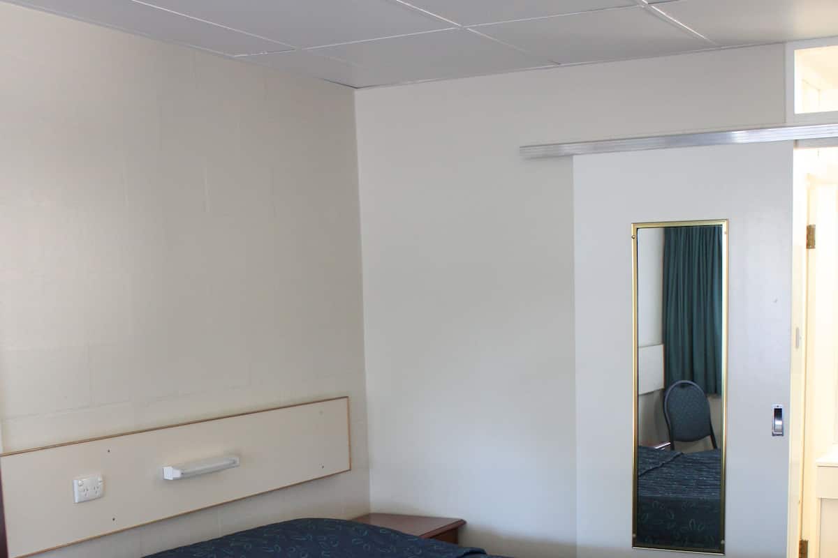 Quarto de hotel com uma cama grande, uma mesa de cabeceira, um espelho e uma porta com cortina.