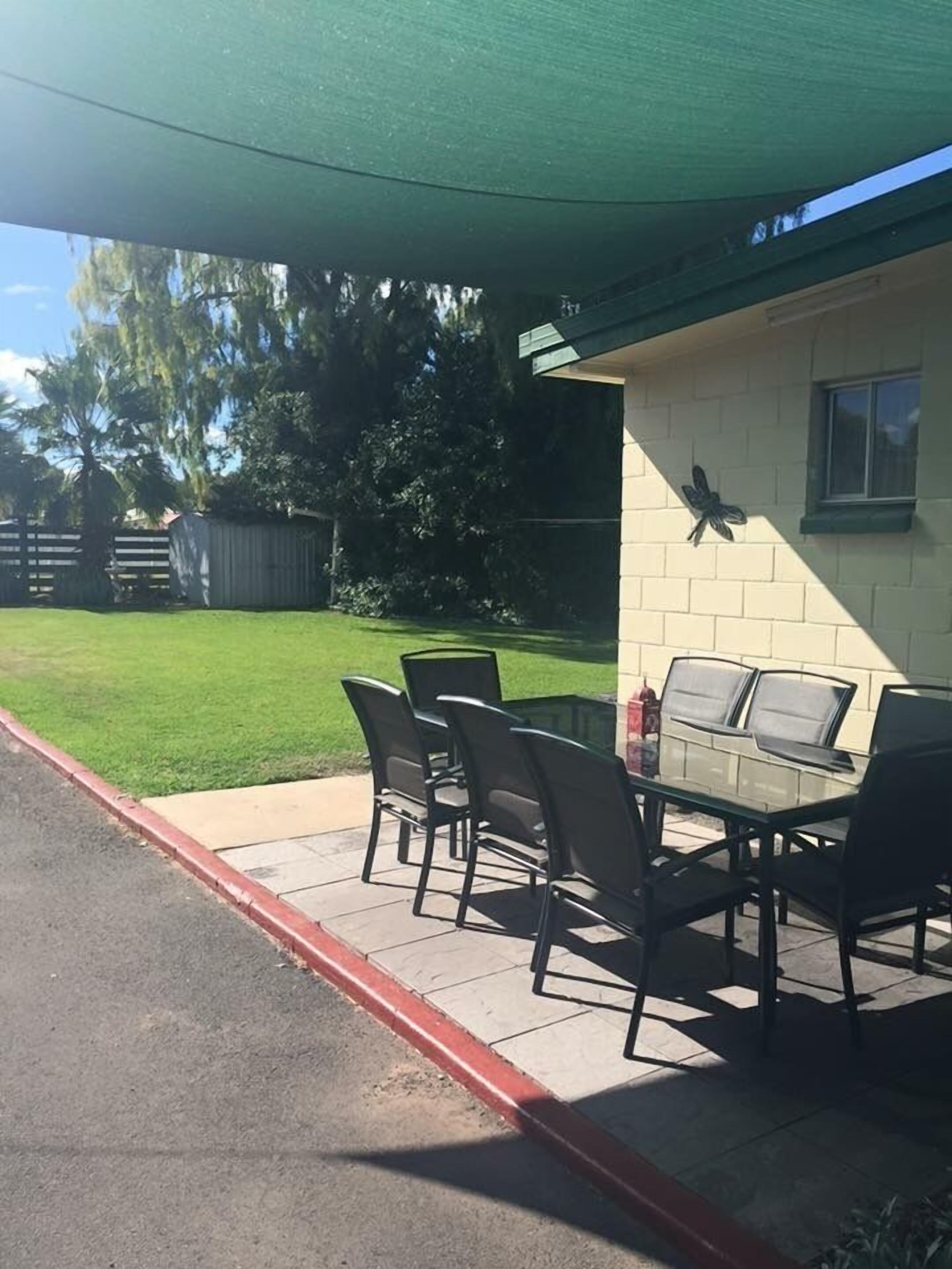 A patio with a table and chairs, a butterfly decoration on the wall, and a green canopy overhead.