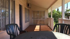 A covered patio with a table and chairs, large windows, and a sliding glass door.