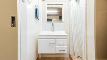 Un pasillo estrecho con un baño blanco que incluye un lavamanos, espejo y toallero.