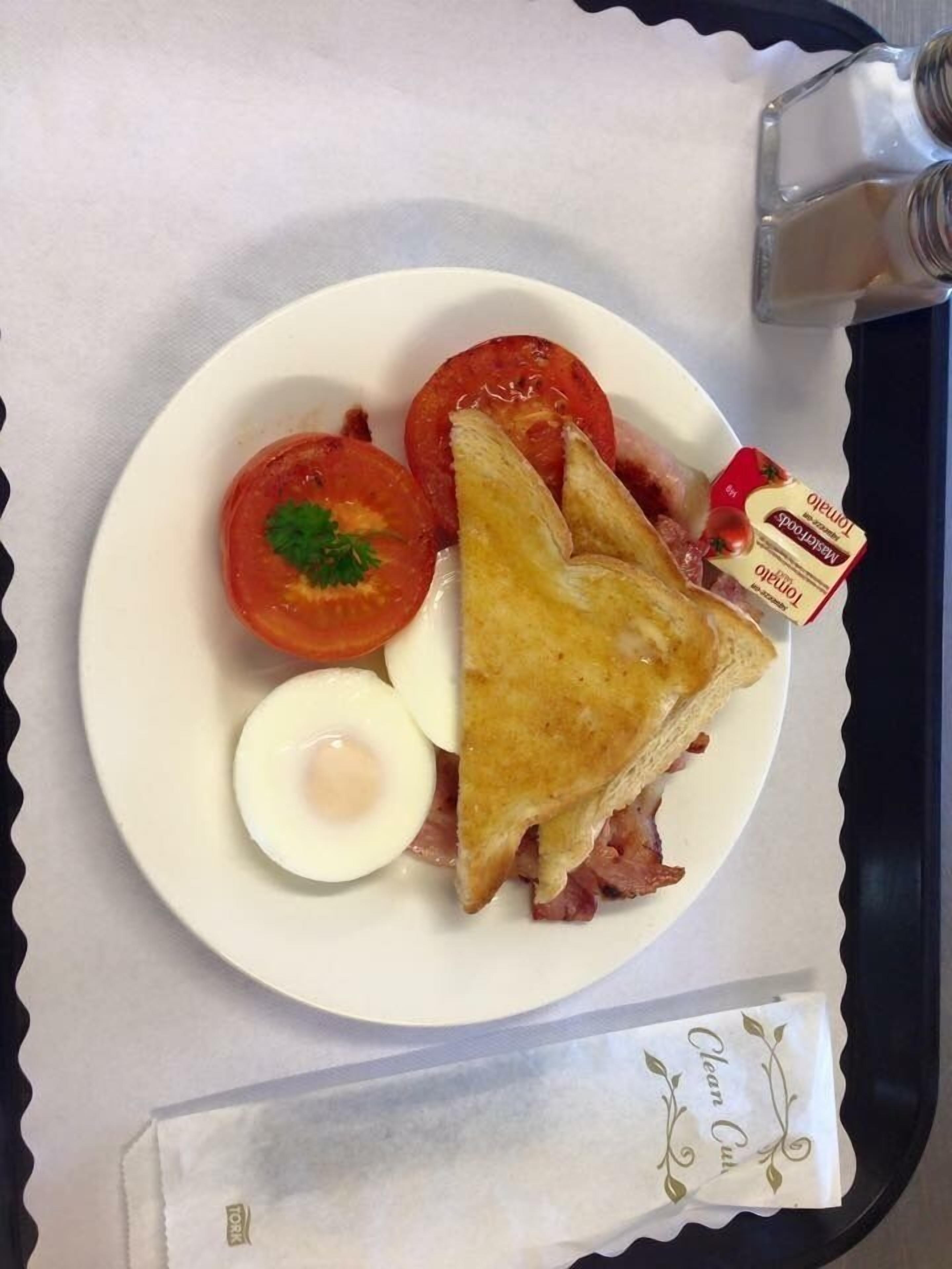 A plate with a sandwich, a boiled egg, and two tomatoes on a white plate.
