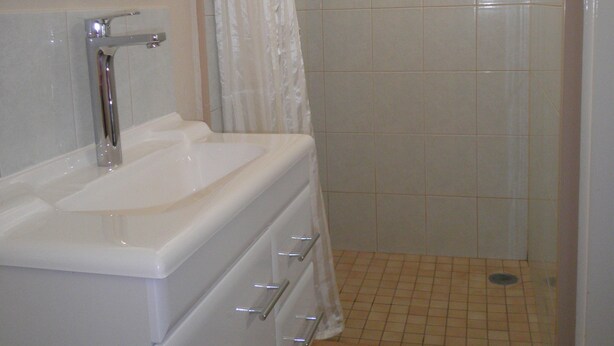 A bathroom with a sink, mirror, shower, and tiled floor. - Roma Motel (Roma)