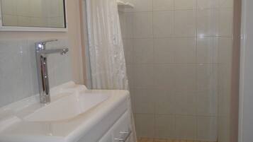 A bathroom with a sink, mirror, shower, and tiled floor.