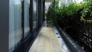 Un pasillo con amplias ventanas, piso de madera y vistas a edificios altos y zonas verdes.