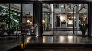 Un interior moderno con puertas de cristal que dan a un comedor con sillas y mesas, rodeado de plantas y una escalera.