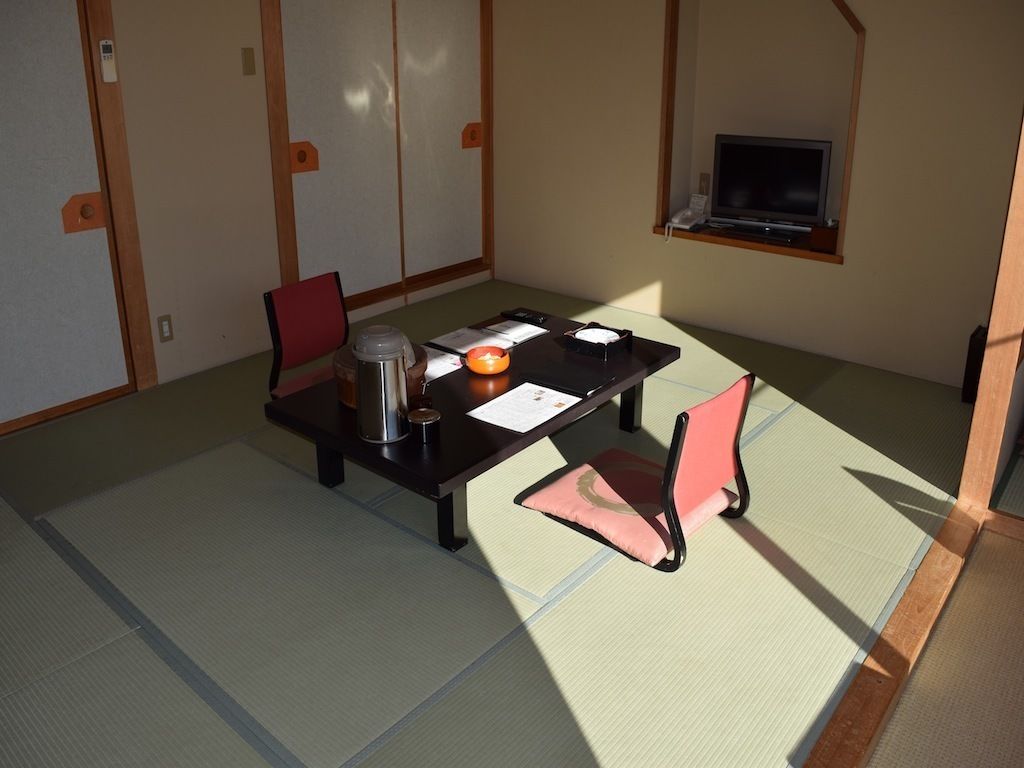 Una habitación con tatami, una mesa baja, dos sillas, un televisor y una puerta corredera.