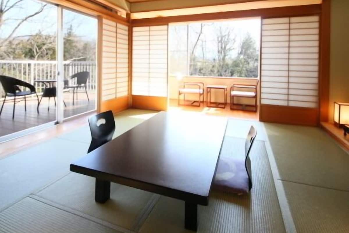 Une pièce dotée d’une grande table en bois, de tatamis, de portes coulissantes et offrant une vue sur l’extérieur.